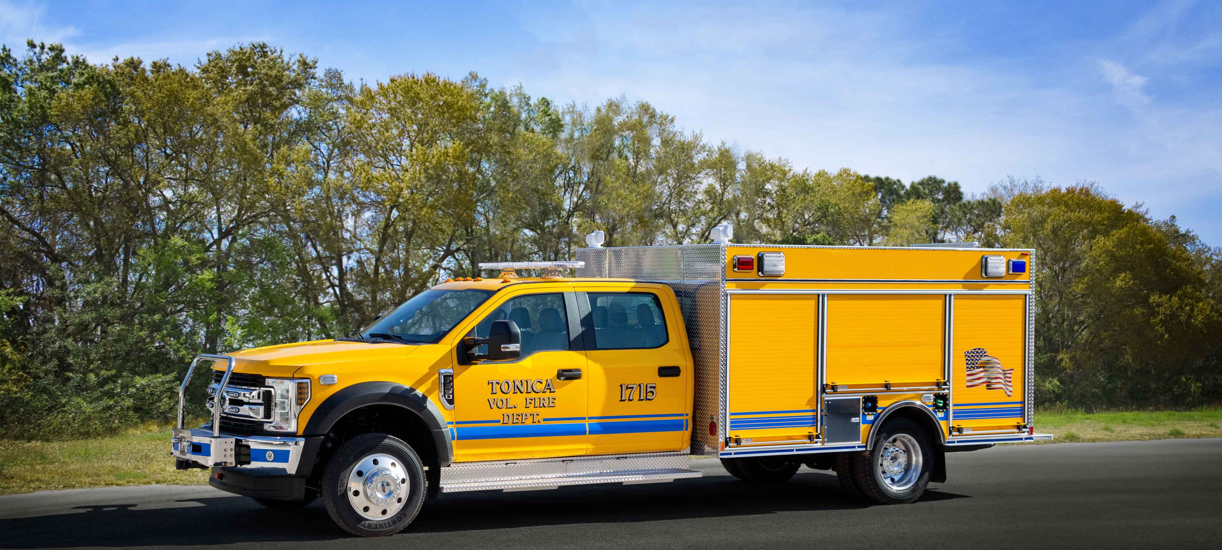 Exterior drivers side of Pierce Ford commercial fire truck chassis parked outside on the road near trees. 