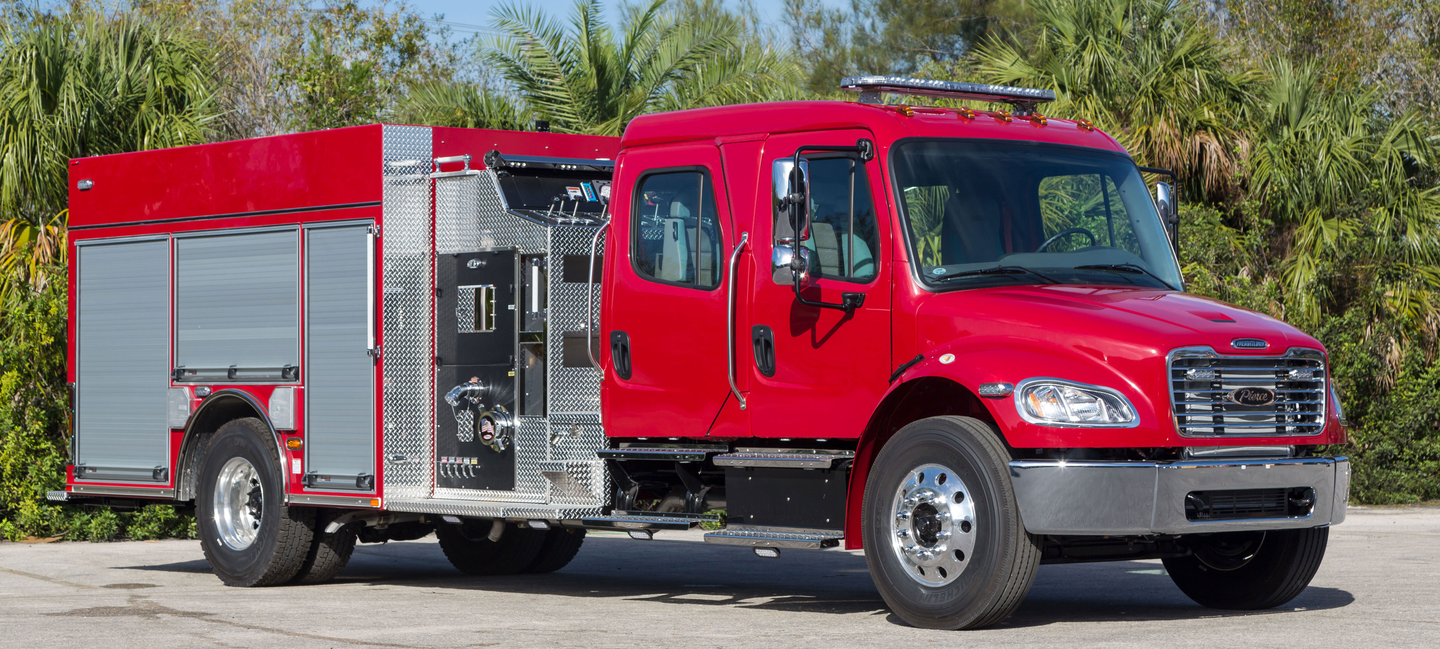 Exterior passengers side of a Pierce Freightliner commercial fire truck chassis parked outside near trees. 