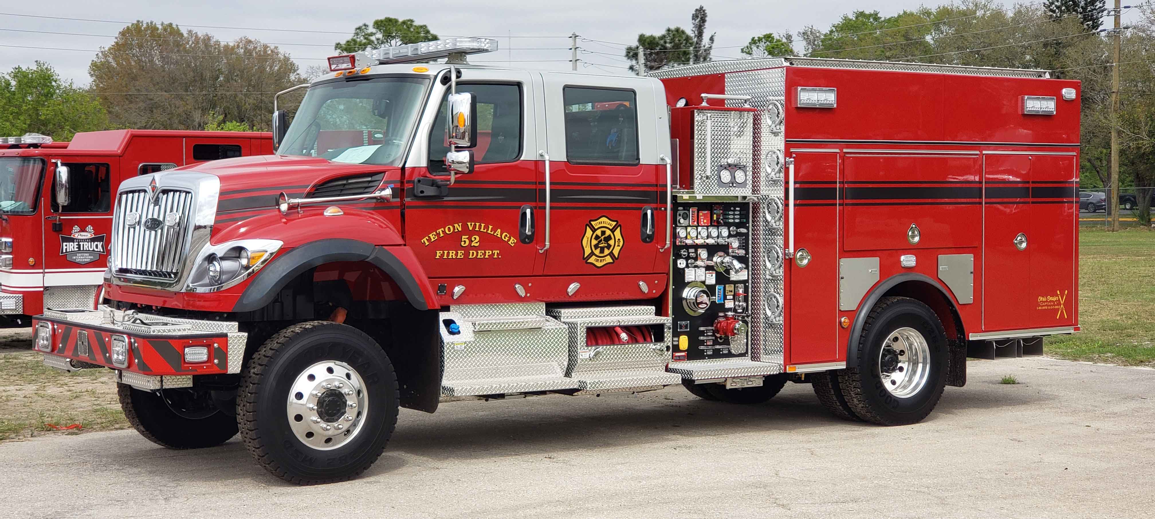 Exterior drivers side of a Pierce International Commercial fire truck chassis parked outside near trees. 