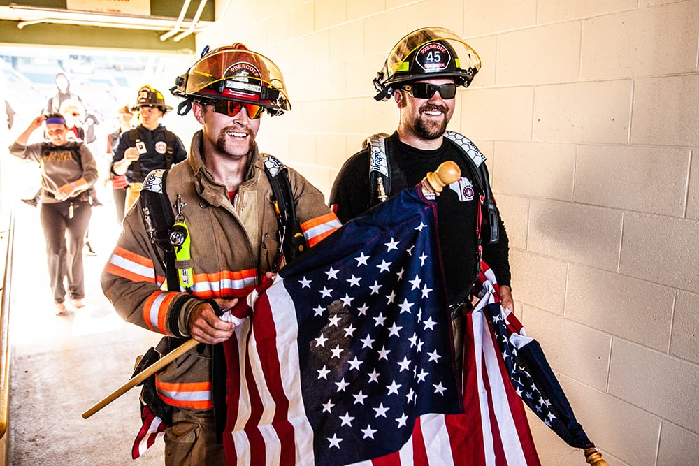 Two Firefighters in turnout gear holding an American Flag walking through the tunnel at Lambeau Field at the Pierce Manufacturing 9/11 Memorial Stair Climb.