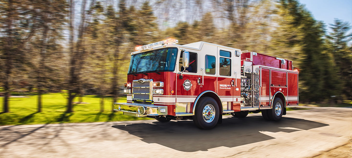 PACCAR MX-13 Big Block Engine in a Pierce Fire Truck driving down the road near trees on a sunny day. 