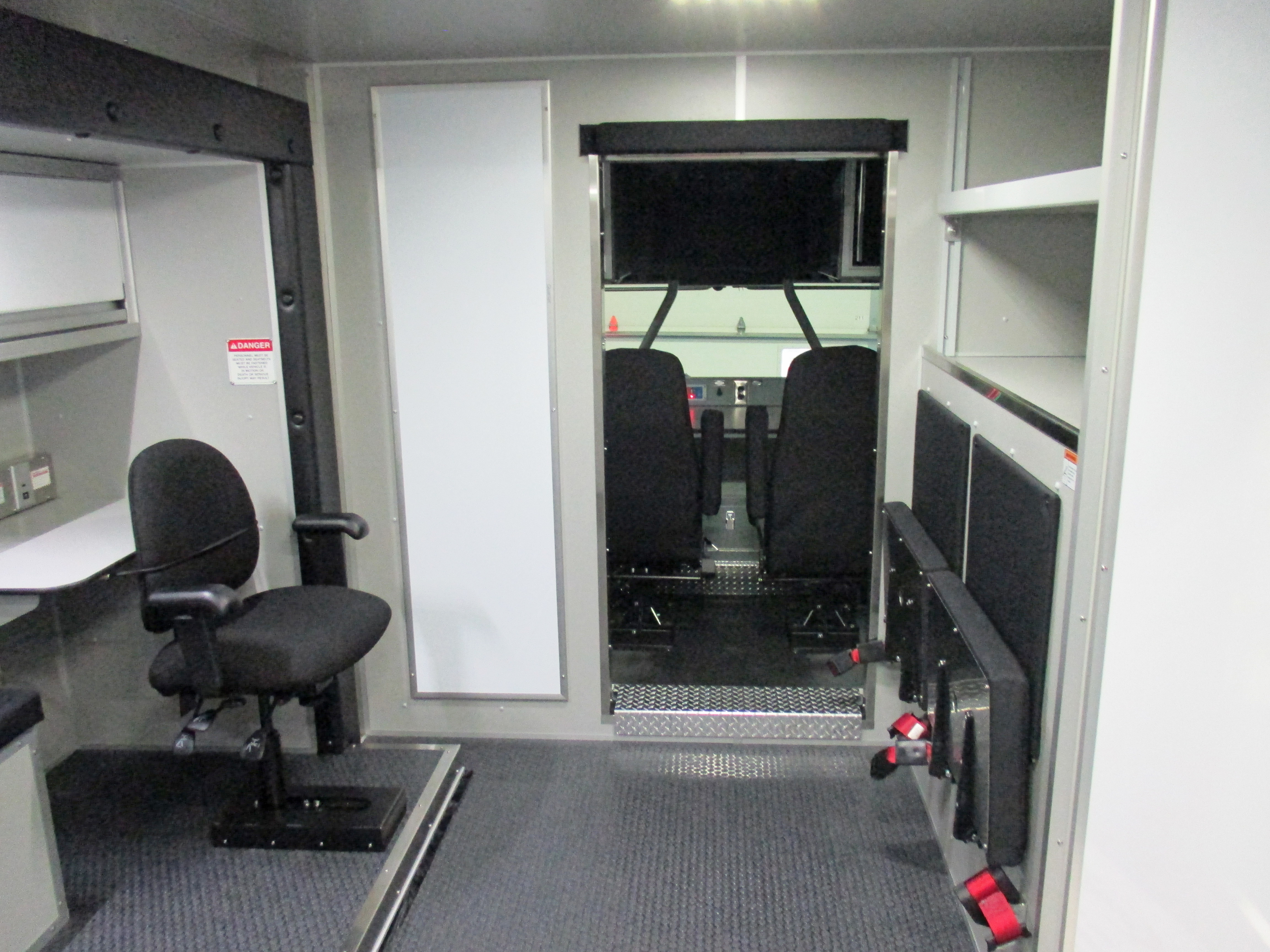 Interior layout of a Pierce Combination Rescue Fire Truck with a desk and chair on the left, compact seating on the right and a door to the controls in the middle.  