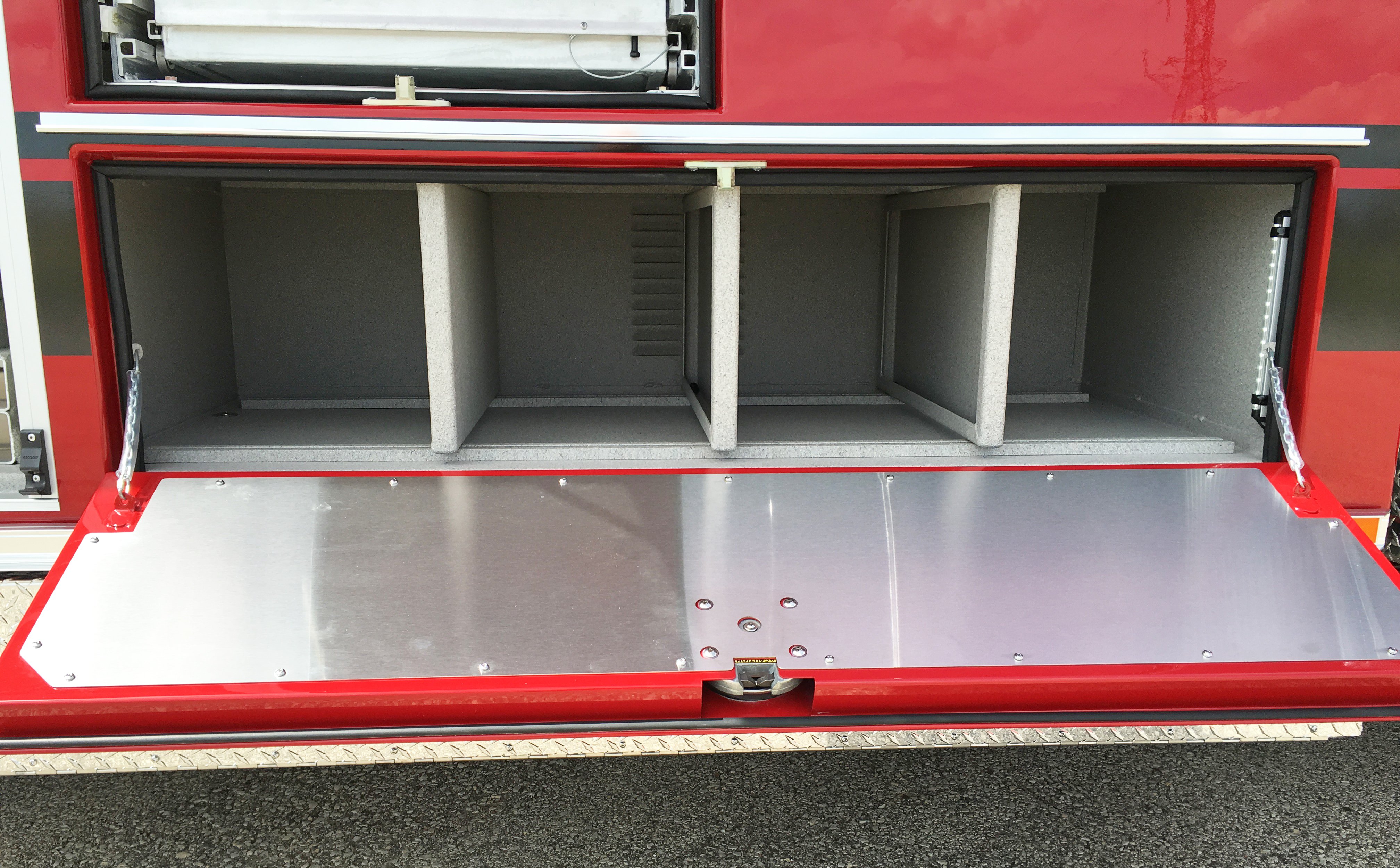 Side of a Pierce Combination Rescue Fire Truck with compartment door open showing four storage spaces. 