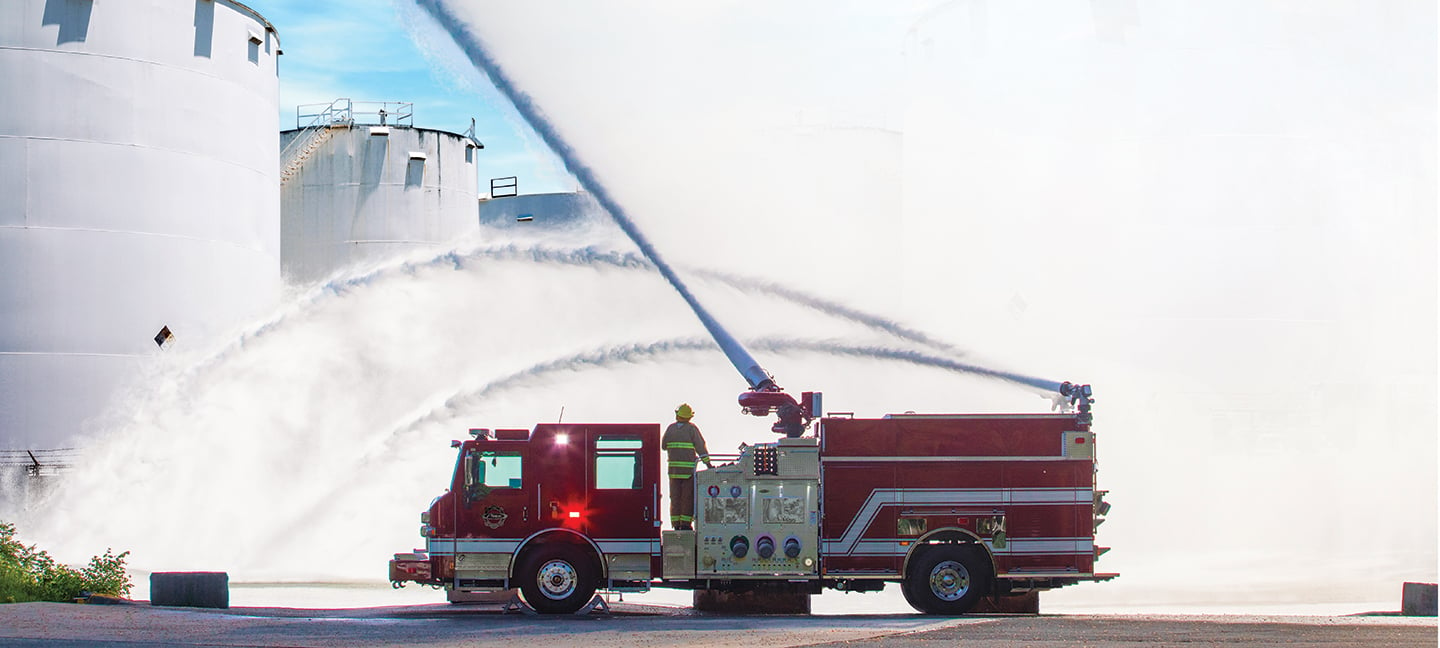 Pierce High Flow Industrial Apparatus Pumper Fire Truck parked outside spraying water out of water pumps near three white farm silos. 