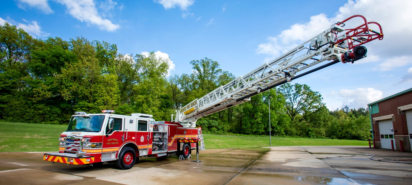 Pierce Aerial Ascendant Fire Truck parked outside next to a fire Department with the ladder ascending into the sky.  