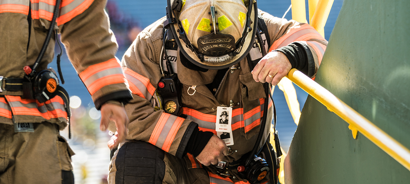 A Firefighter in turnout gear kneeling at the steps of Lambeau Field at the Pierce Manufacturing 9/11 Memorial Stair Climb event.