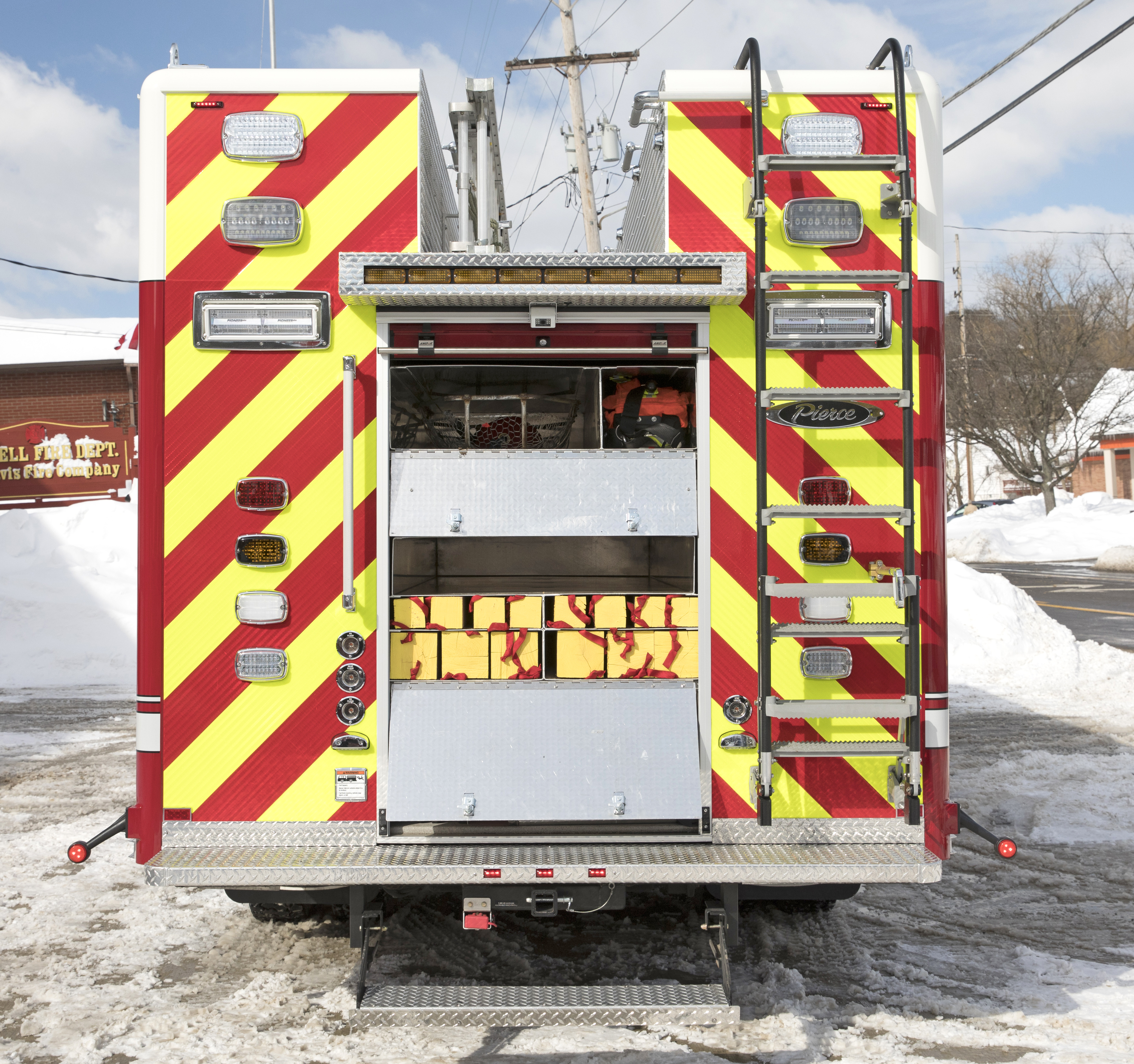 Rear of a Pierce Non-Walk-In Heavy-Duty Rescue Fire Truck parked outside on a snowy day with compartments open showing storage space. 