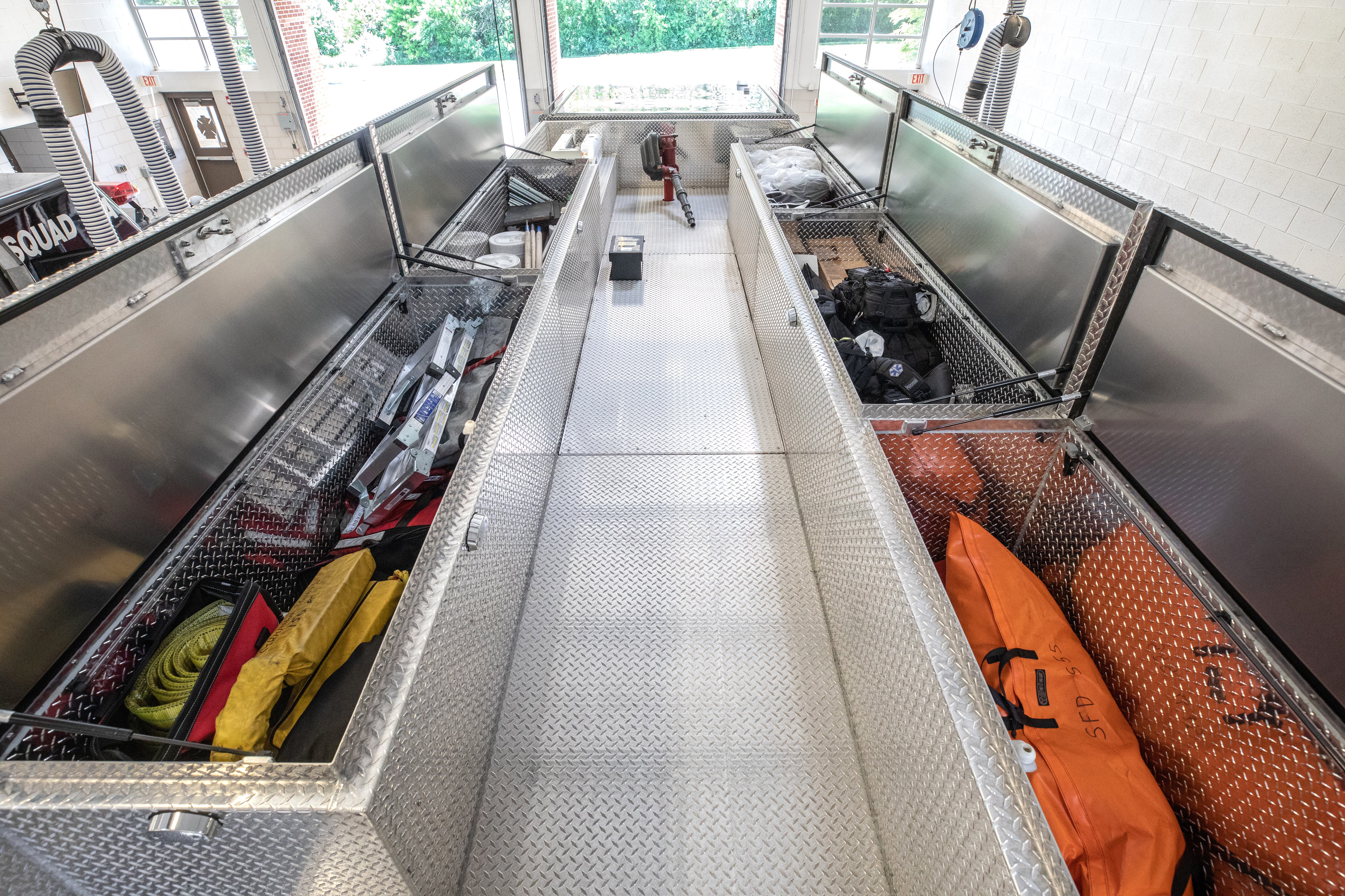 The top of a Pierce Non-Walk-In Rescue Fire Truck with storage compartments on the left and right sides parked inside of a fire station. 