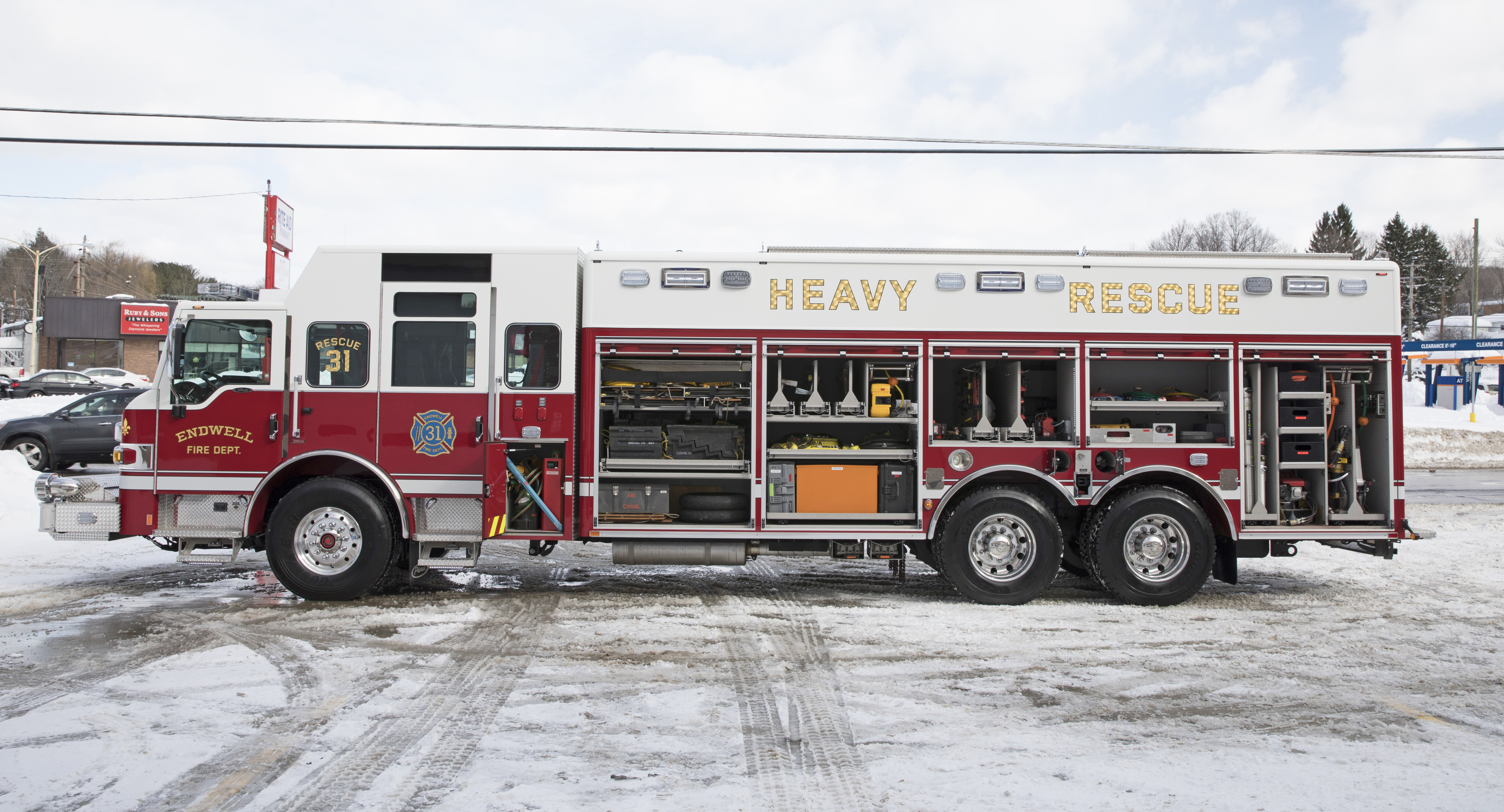 Driver’s side of a Pierce Non-Walk-In Rescue Fire Truck parked outside on a snowy day with side compartments open showing storage space. 