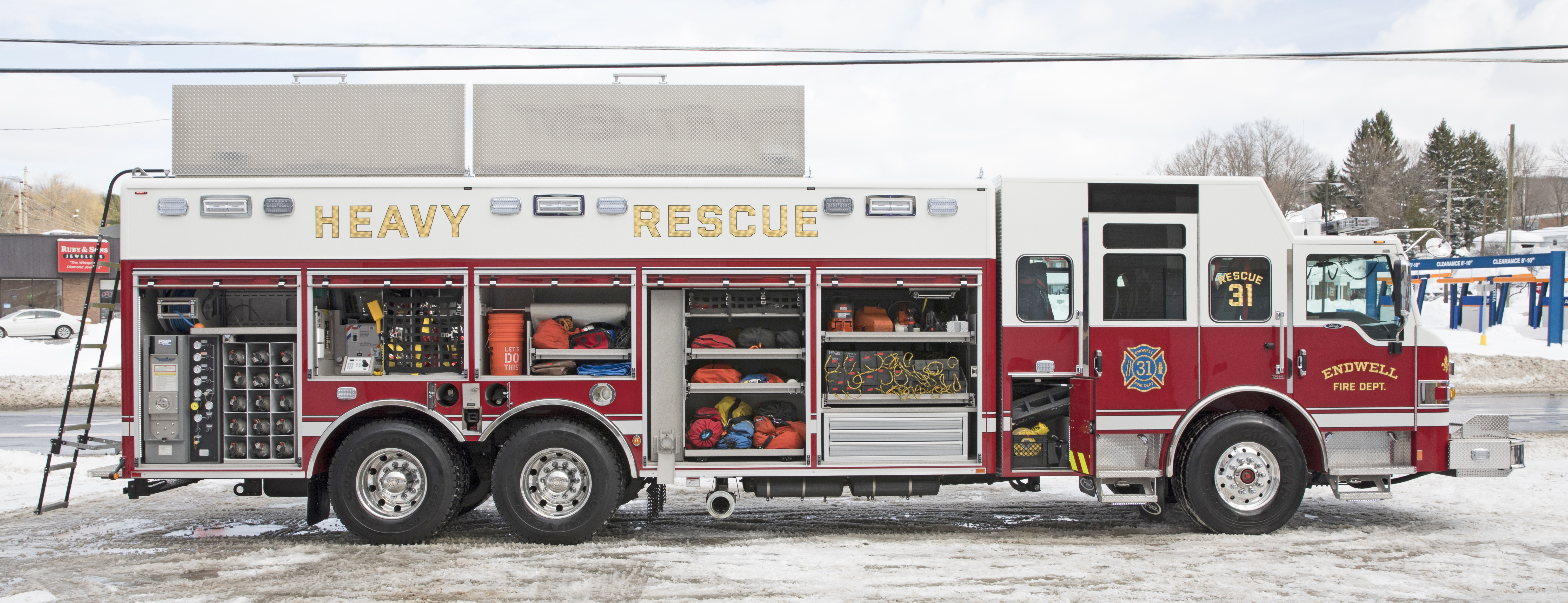 Passenger’s side of a Pierce Non-Walk-In Rescue Fire Truck parked outside on a snowy day with compartments open showing storage space. 