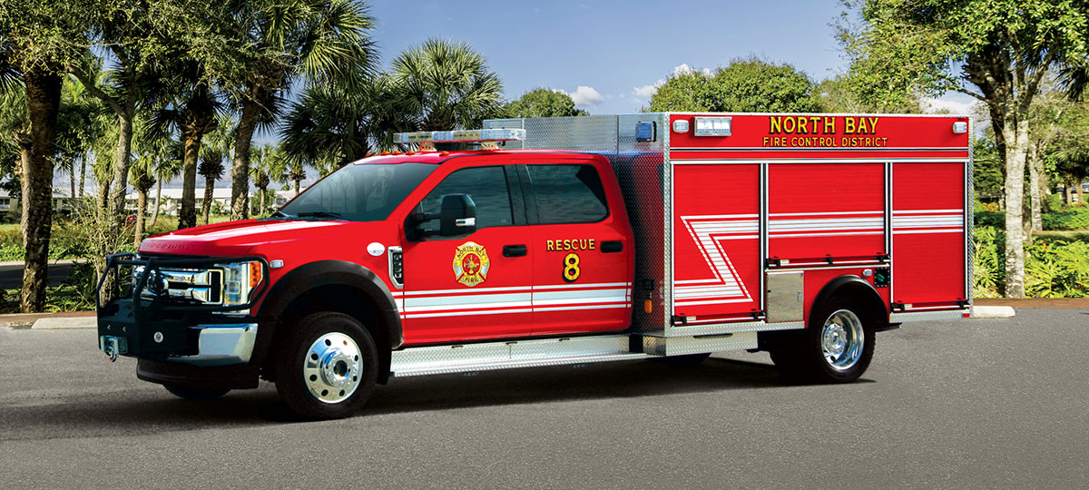 Pierce Mini Pumper Fire Truck parked outside in a parking lot near trees on a sunny day. 