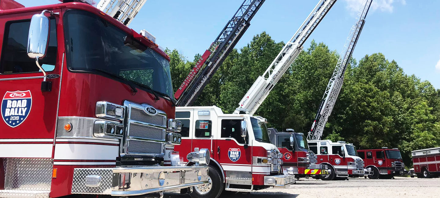 Pierce Fire Trucks with ladders ascending into the air outside on a sunny day at a Pierce Road Rally Event.