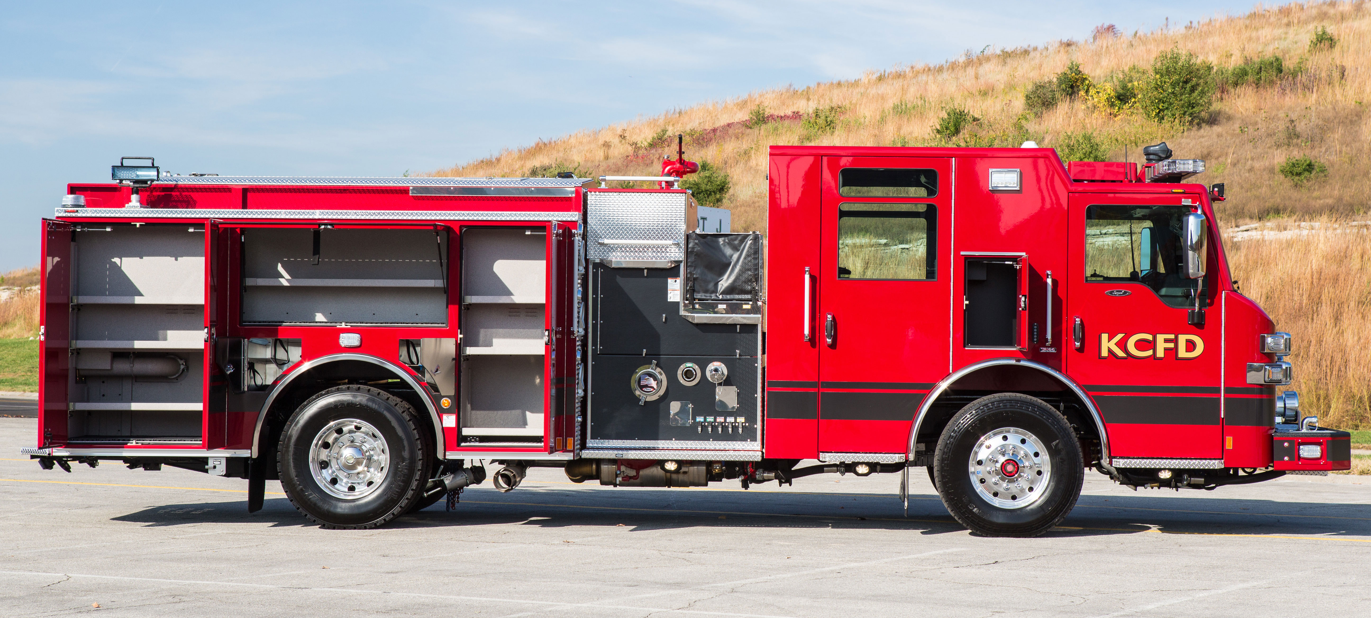 Passenger’s side of a Pierce Pumper Fire Truck parked outside with side compartments open showing storage space. 