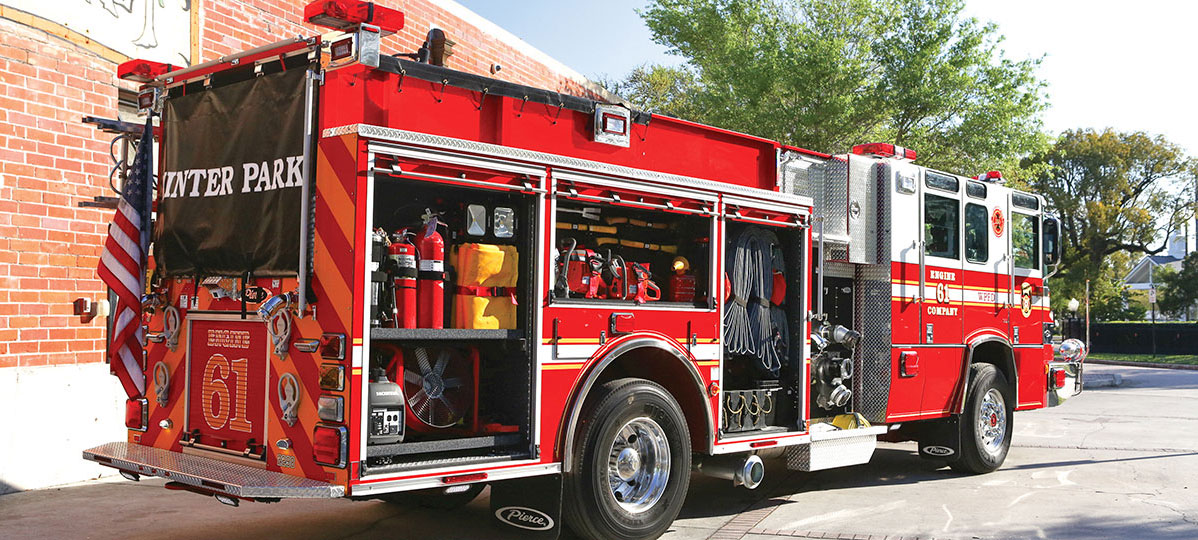 Pierce Pumper Fire Truck parked outside in front of Fire Station with side compartments open showing versatile storage options. 