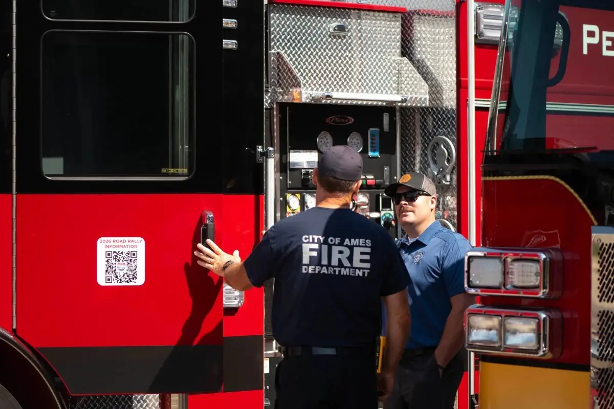 A firefighter from the City of Ames Fire Department stands by a Pierce fire truck with a 2026 Road Rally QR code.