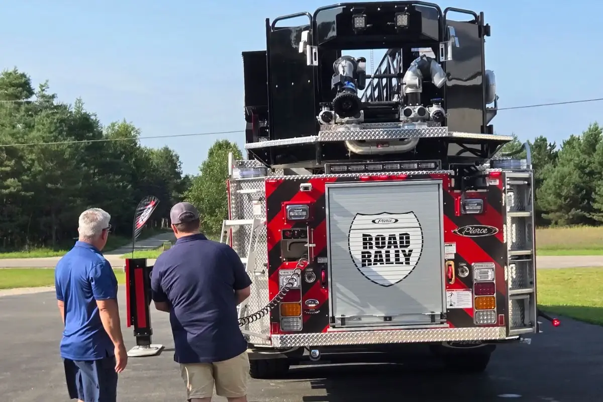 Two men look at a Pierce fire truck displaying the Road Rally logo on its rear roll-up door.