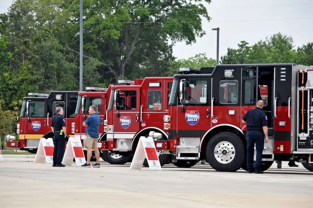 Firefighters and visitors stand near a lineup of custom Pierce fire trucks at a Road Rally event.