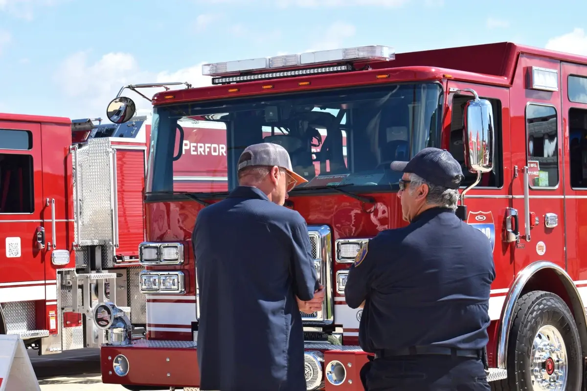 Two men discuss fire truck features in front of a red fire apparatus at a Pierce Road Rally event.