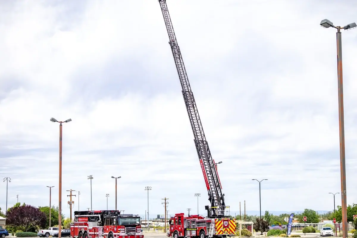 Two red Pierce fire trucks on display in a parking lot, with one showcasing a fully extended aerial ladder.