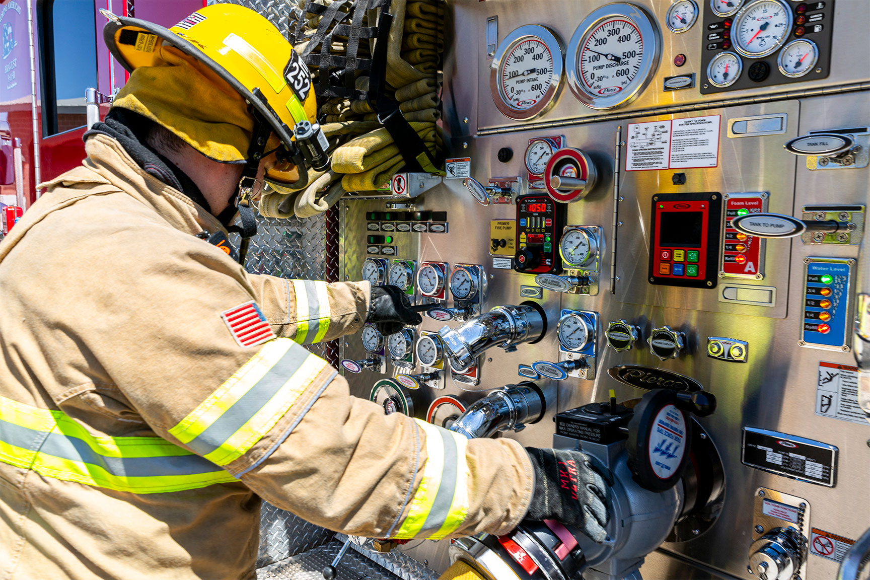 A firefighter in turnout gear working at a pump panel on a Volterra electric fire truck.