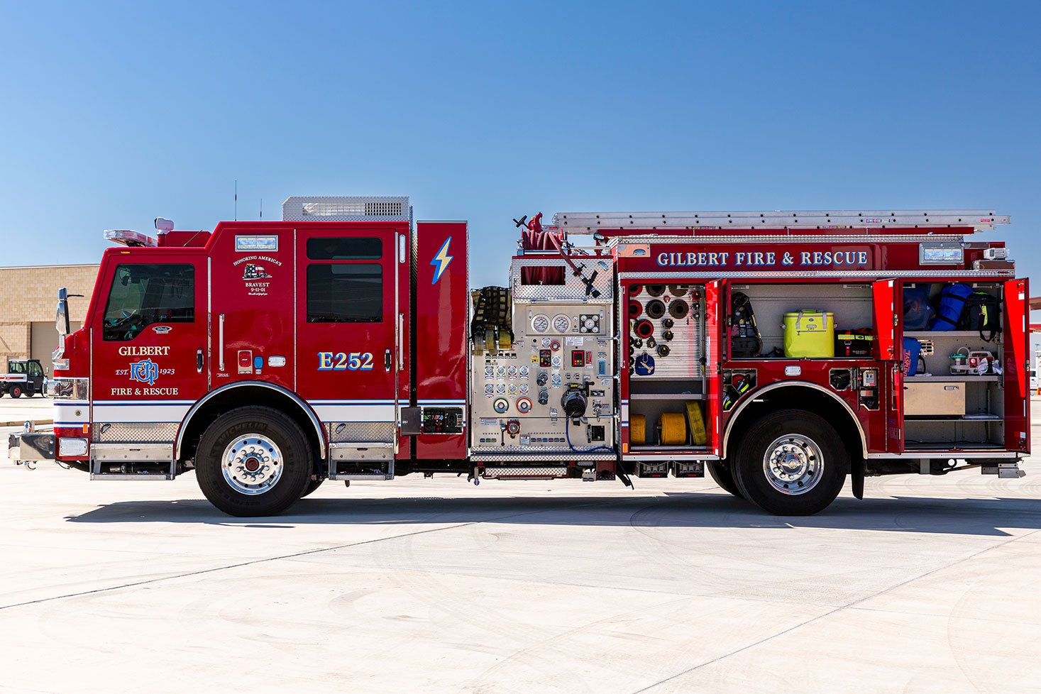 The drivers side of an electric fire truck with the compartments open showing tools and equipment inside on a sunny day.