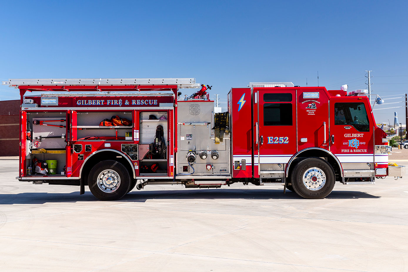 The officers side of an electric fire truck with the compartments open showing tools and equipment inside on a sunny day.