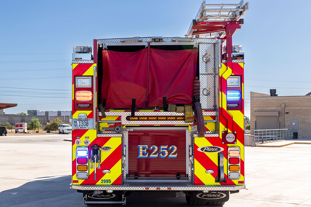 The rear of a Volterra Pumper with hose in the hosebed covered with a red cover and ground ladders stored on a hydraulic rack.