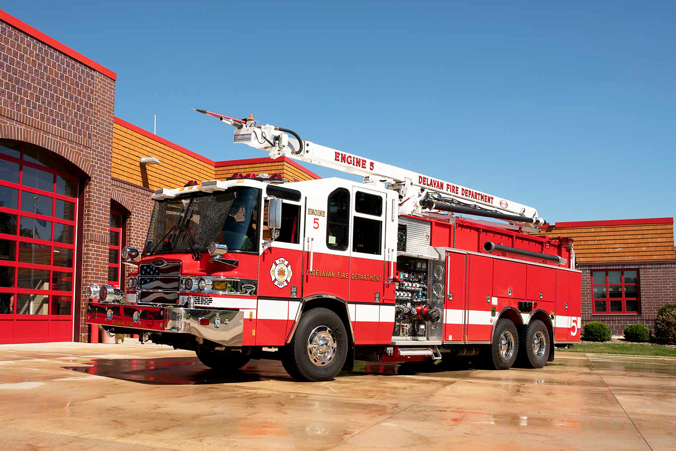 Pierce Fire Truck with a high-reach extendable snozzle parked outside on a sunny day in front of a Fire Station. 