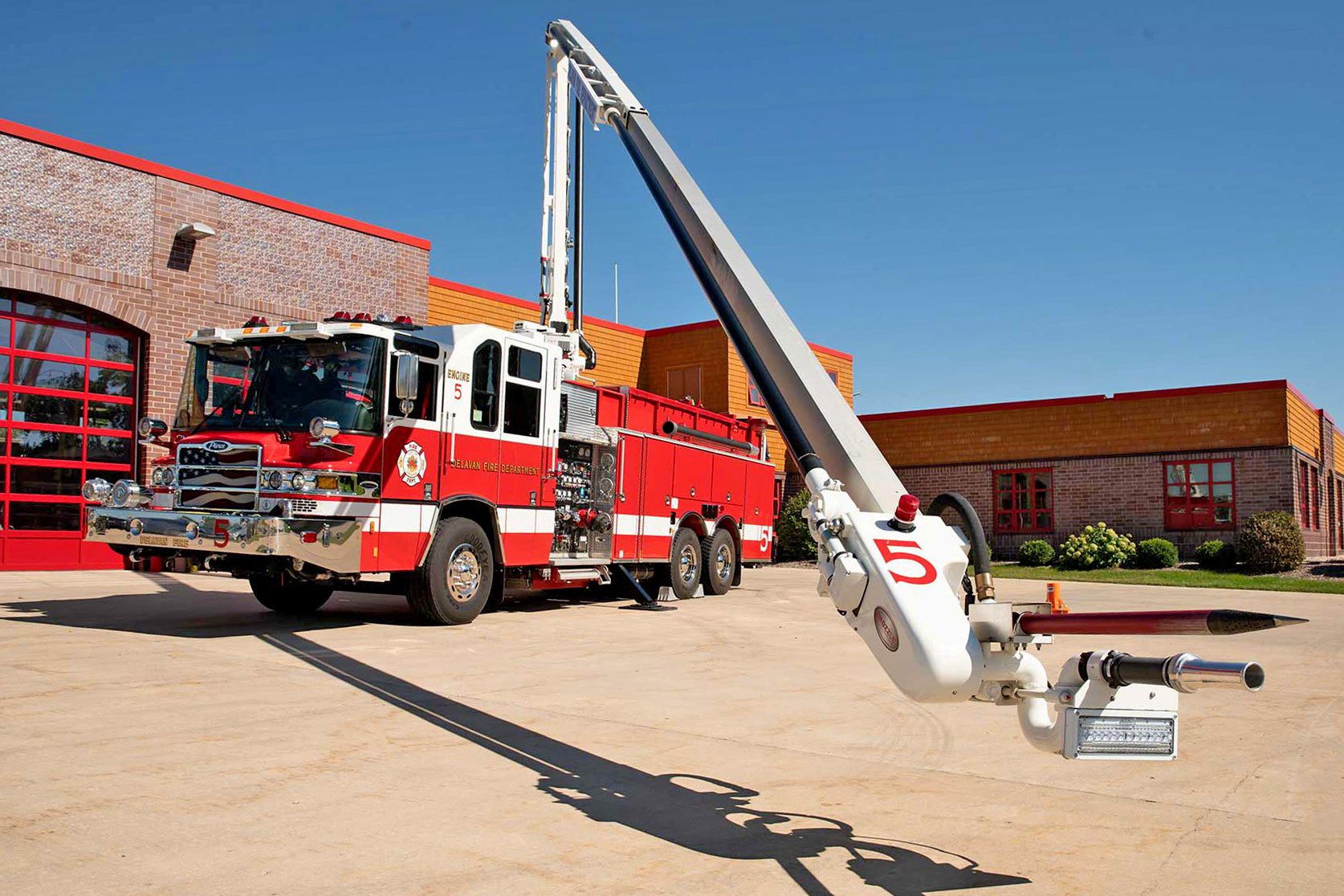 Pierce Fire Truck parked outside on a sunny day in front of a Fire Station with the High-Reach Snozzle extended out in front of the truck. 