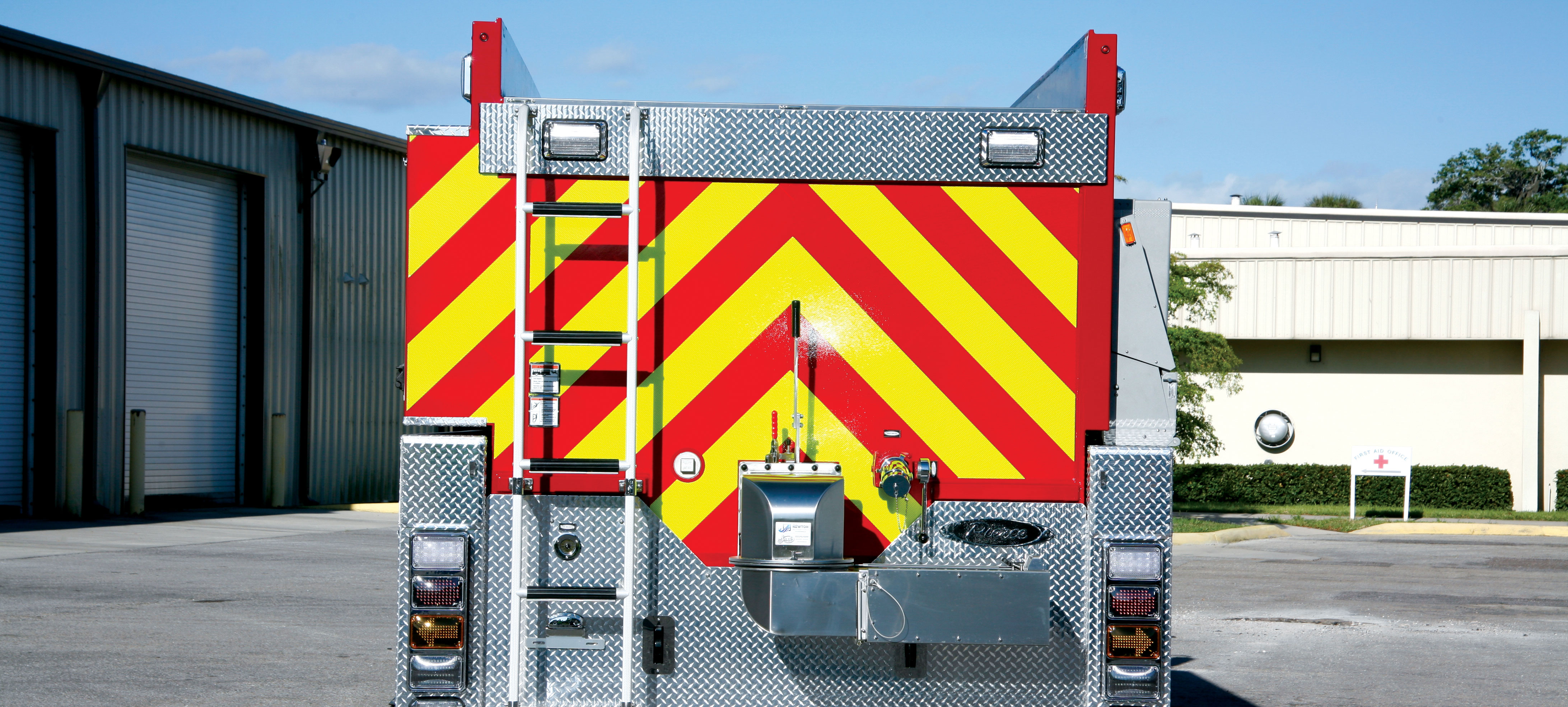 Rear of a Pierce Tanker Fire Truck parked outside in a parking lot near a building with Swivel Dump Valve and Safe Access to the hose bed. 