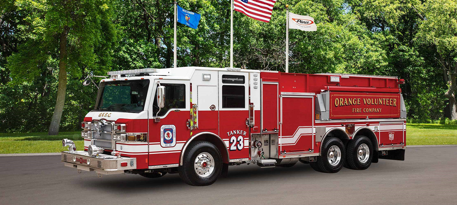 Pierce PUC™ Tanker Fire Truck parked outside near trees and three flags on a sunny day. 