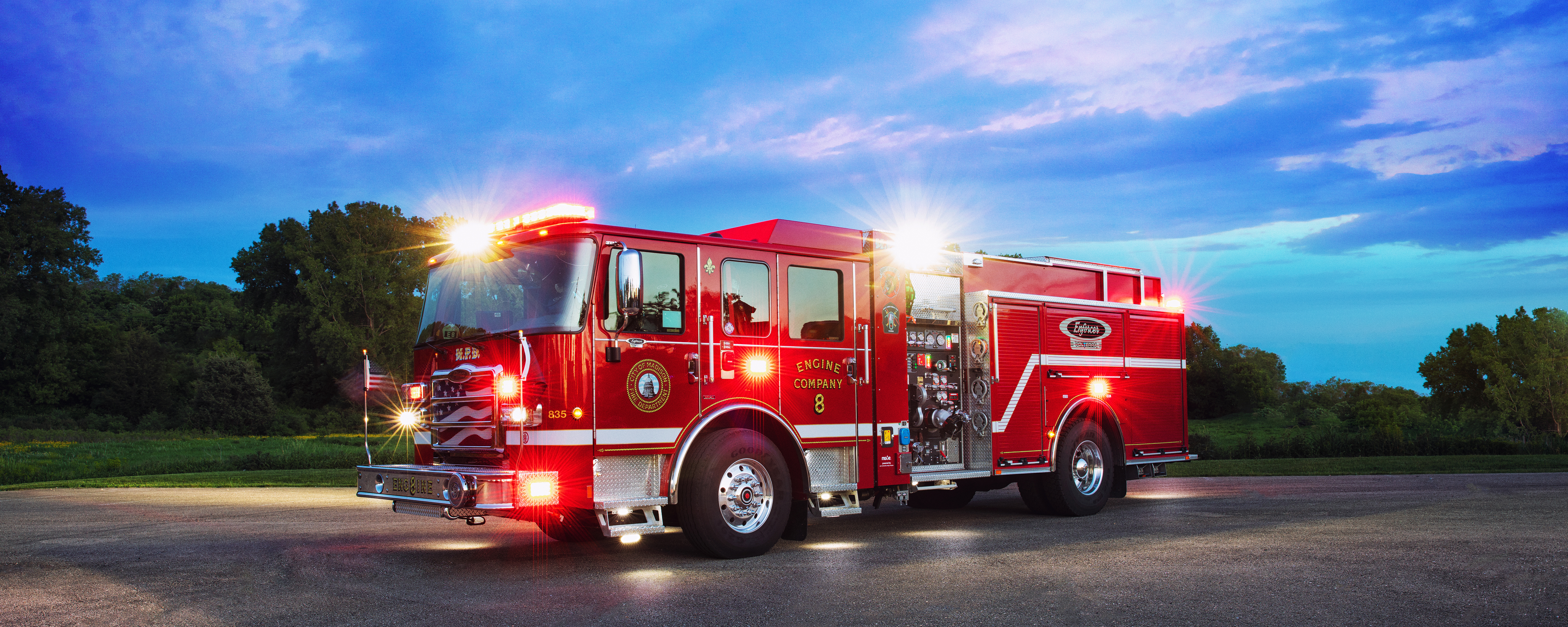 Pierce Volterra electric fire truck parked in Madison, Wisconsin at dusk with emergency lights on. 