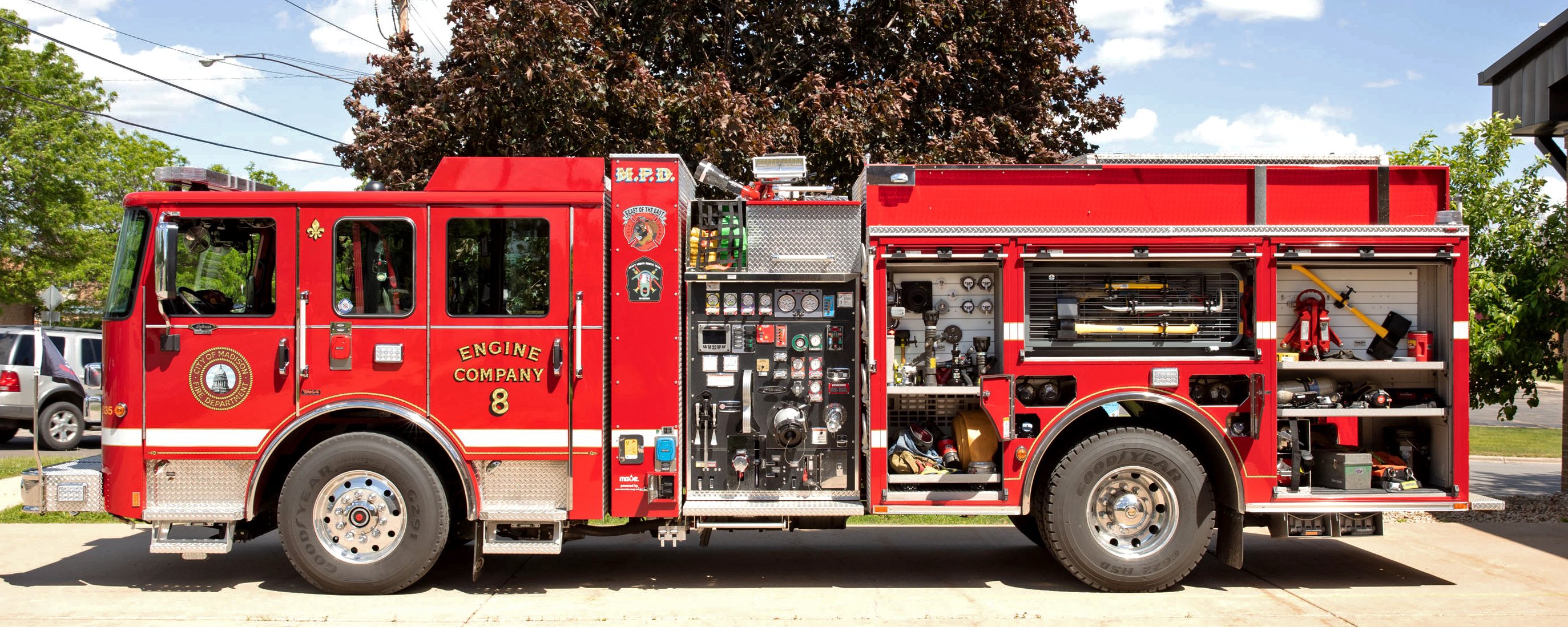 Pierce Volterra electric fire truck parked on the street with drivers side compartment doors open showing compartments and storage space. 