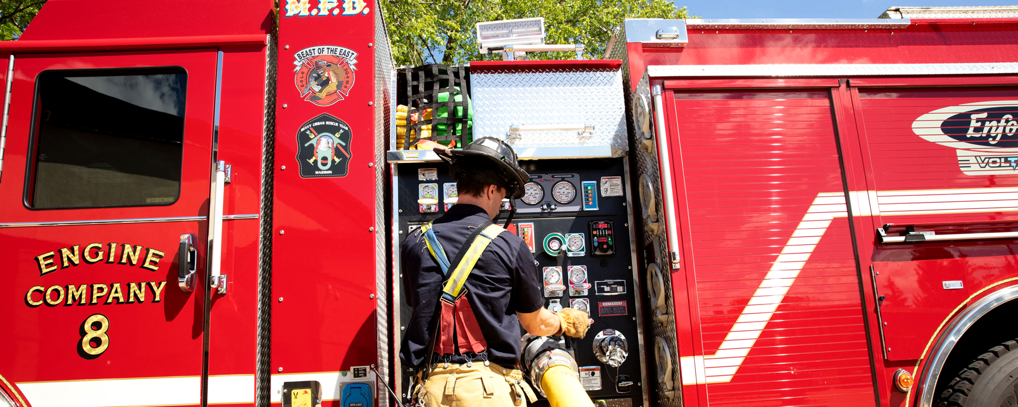 Firefighter pumping water from the pump house with a hose through the Pierce Enforcer Volterra electric vehicle. 