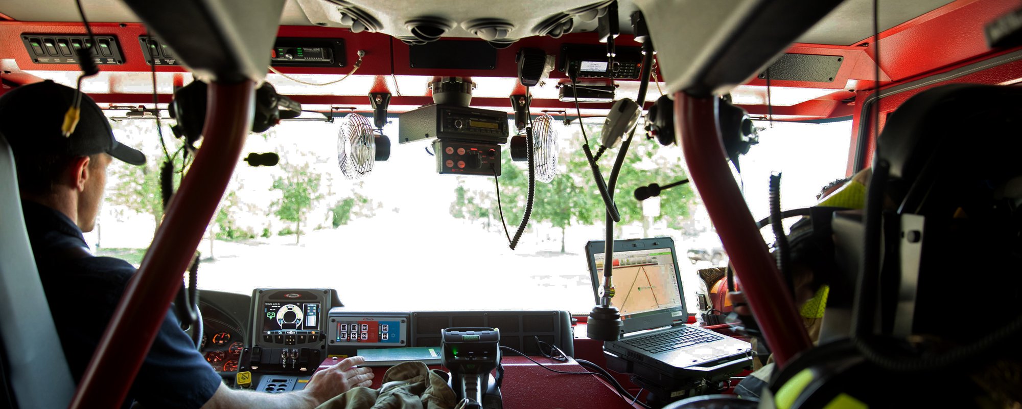 Two people in the interior of a Pierce Volterra electric fire truck looking out from the windshield. 