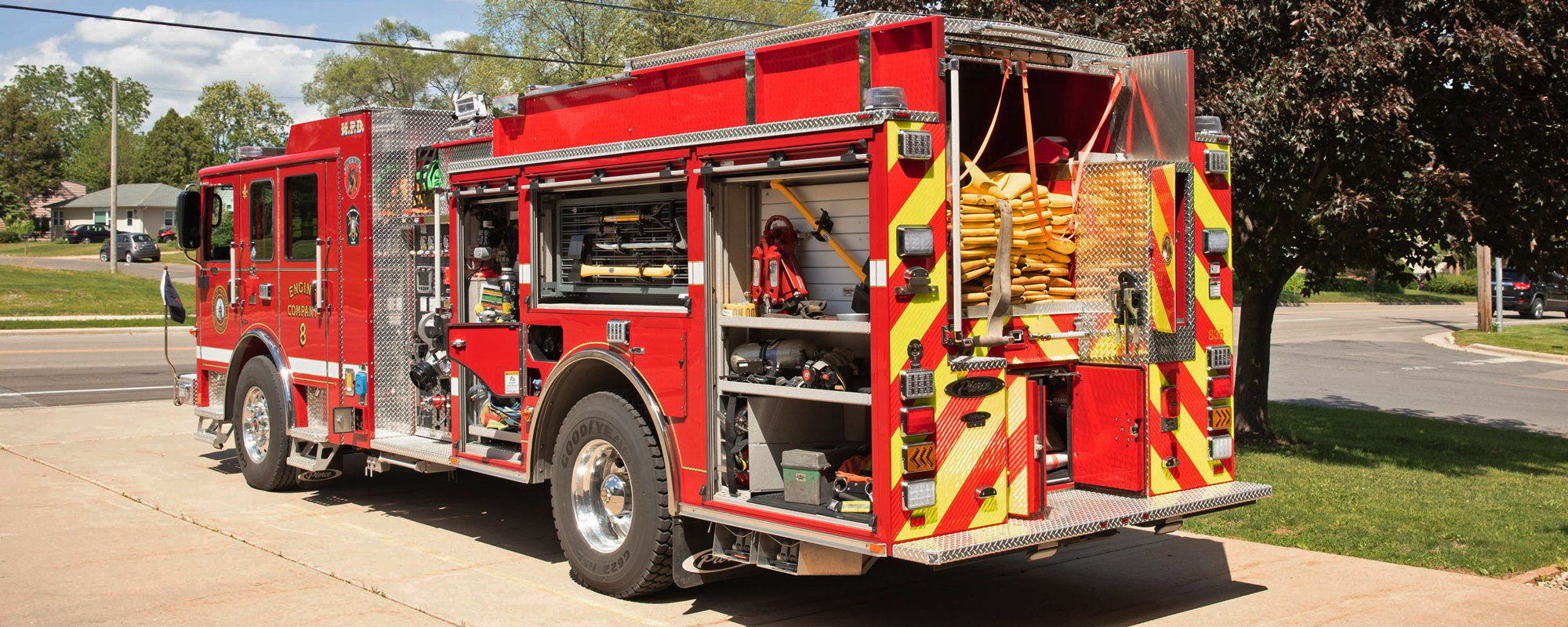 Pierce Volterra electric fire truck parked outside with the drivers side and rear compartment doors open on a sunny day. 