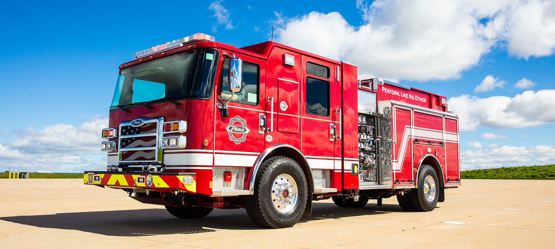 The front drivers side of a Pierce Volterra Electric Fire Truck parked on a sunny day with clouds in the sky.