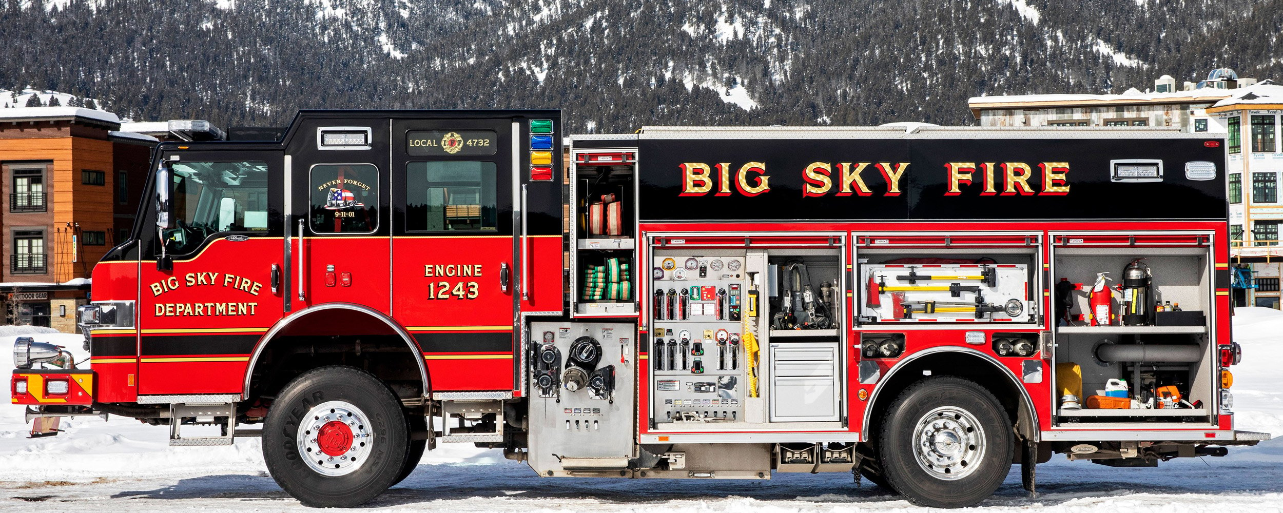 Pierce Pumper Fire Truck with side storage compartments open parked outside on a snowy day near mountains. 